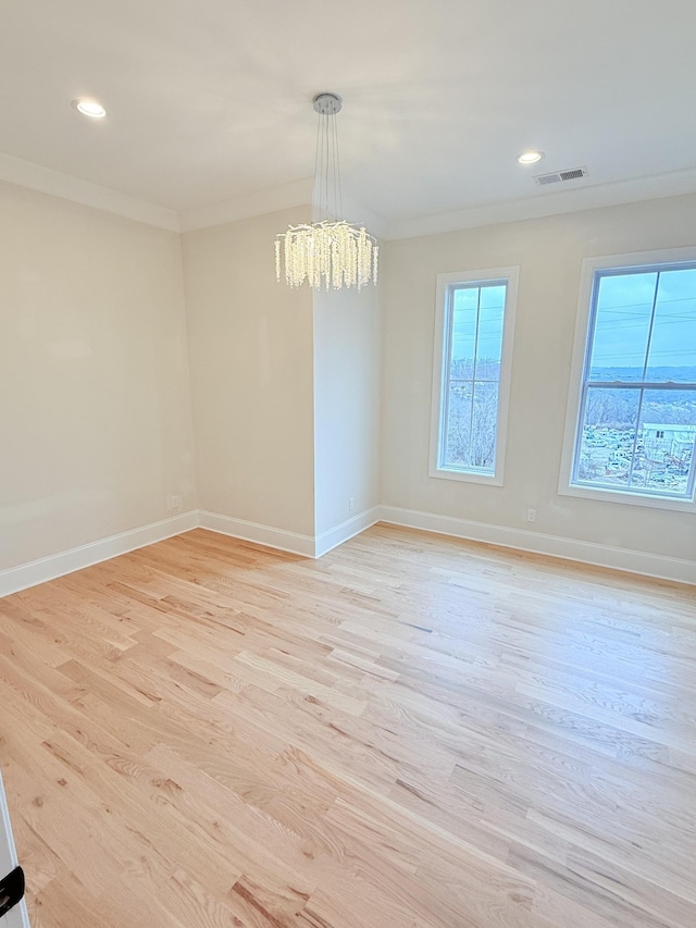 empty room with crown molding, a notable chandelier, and light wood-type flooring