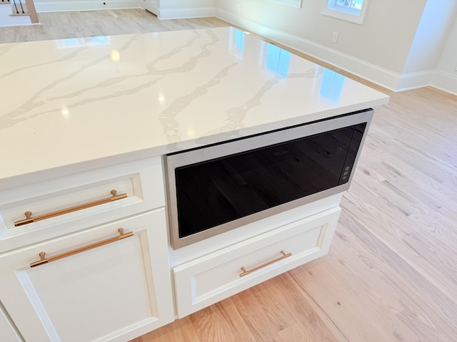 room details with light wood-type flooring, white cabinets, and light stone counters