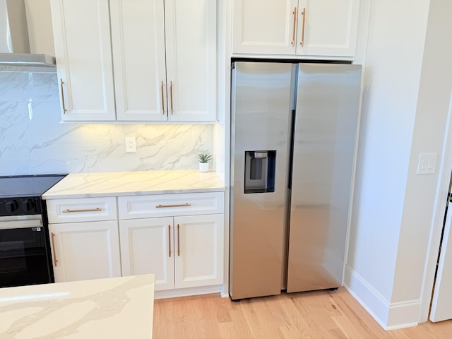 kitchen featuring stainless steel refrigerator with ice dispenser, black range with electric cooktop, wall chimney range hood, light stone countertops, and white cabinets