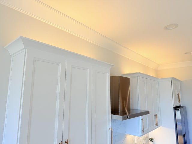 details with ornamental molding, white cabinets, refrigerator, and wall chimney exhaust hood