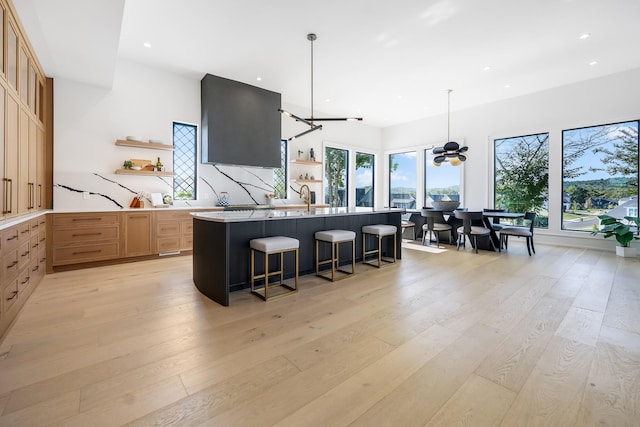 kitchen featuring a breakfast bar area, light stone counters, light hardwood / wood-style flooring, pendant lighting, and a kitchen island with sink