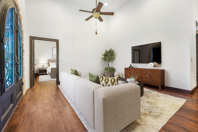 living room with dark wood-type flooring, ceiling fan, and a high ceiling