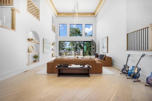 living room with ornamental molding, a high ceiling, built in features, and light wood-type flooring