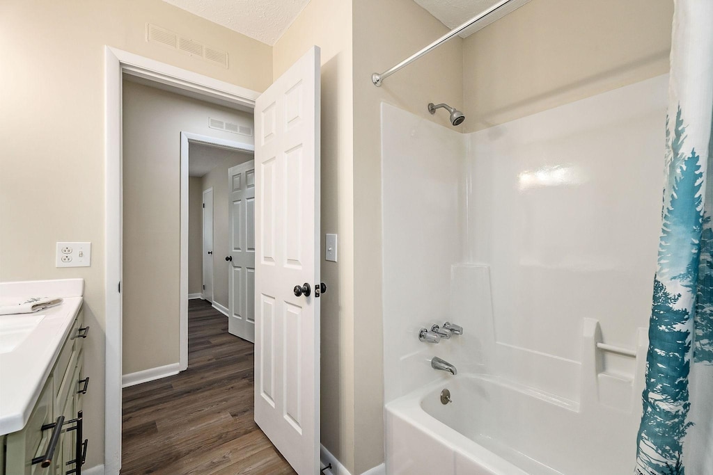 bathroom with hardwood / wood-style flooring, vanity, and shower / bathtub combination with curtain