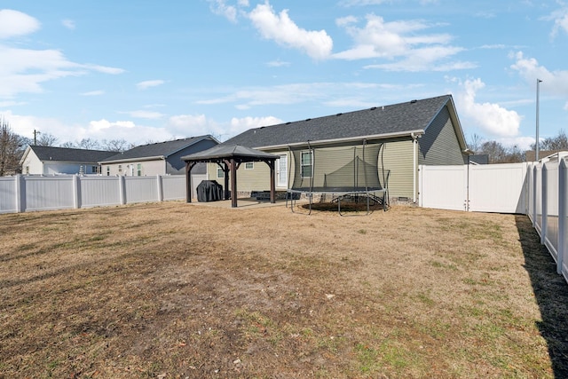 rear view of property featuring a gazebo, a trampoline, and a lawn