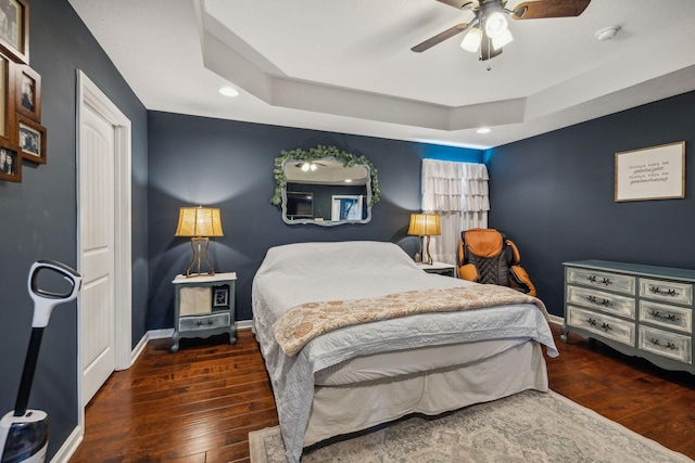 bedroom with ceiling fan, dark hardwood / wood-style floors, and a raised ceiling