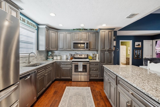 kitchen with stainless steel appliances, sink, dark wood-type flooring, and light stone counters