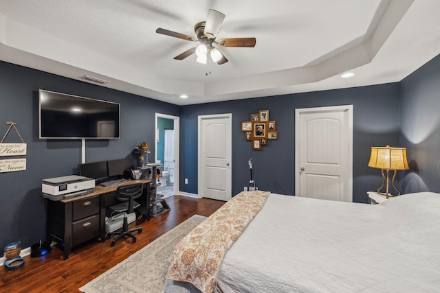 bedroom featuring a raised ceiling, dark wood-type flooring, and ceiling fan