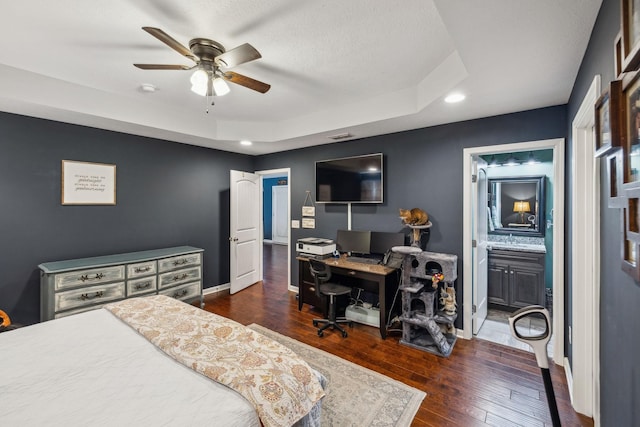 bedroom featuring dark wood-type flooring, ceiling fan, connected bathroom, and a tray ceiling