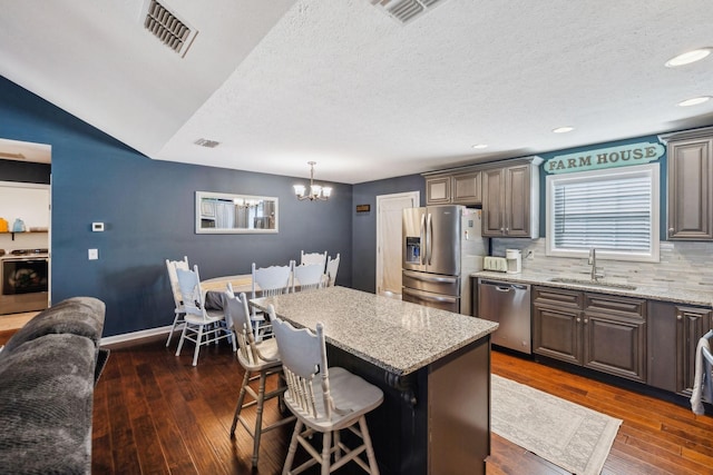 kitchen featuring a kitchen bar, sink, light stone counters, a center island, and appliances with stainless steel finishes