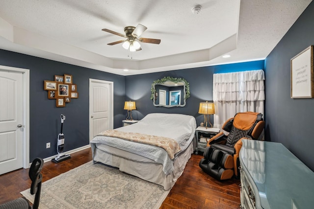 bedroom with ceiling fan, a textured ceiling, dark hardwood / wood-style flooring, and a tray ceiling