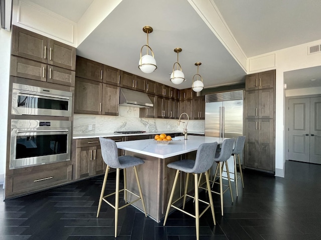 kitchen with appliances with stainless steel finishes, pendant lighting, a kitchen bar, decorative backsplash, and a center island with sink