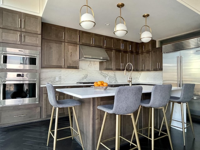 kitchen featuring a kitchen island with sink, backsplash, stainless steel appliances, a kitchen bar, and decorative light fixtures