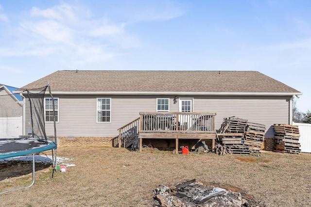 rear view of house featuring a trampoline, a wooden deck, and a lawn