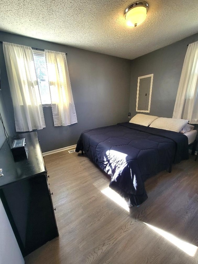 bedroom featuring hardwood / wood-style floors, electric panel, and a textured ceiling