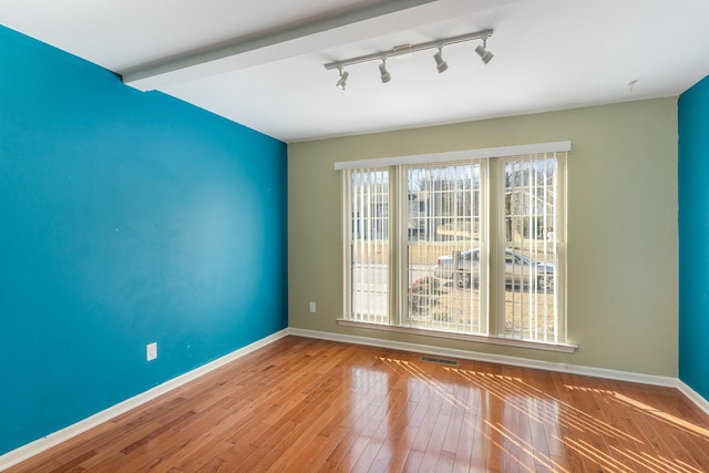 unfurnished room featuring beamed ceiling, rail lighting, and light hardwood / wood-style flooring