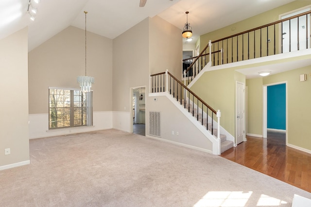 unfurnished living room featuring rail lighting, carpet floors, an inviting chandelier, and high vaulted ceiling