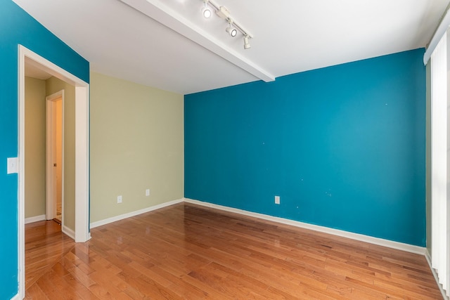 unfurnished room featuring track lighting, beam ceiling, and light hardwood / wood-style flooring