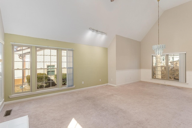 carpeted empty room featuring rail lighting, a chandelier, high vaulted ceiling, and a wealth of natural light