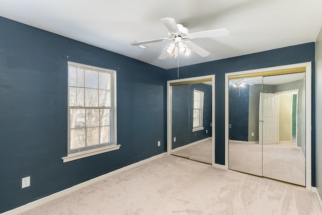 unfurnished bedroom with multiple closets, ceiling fan, and light carpet