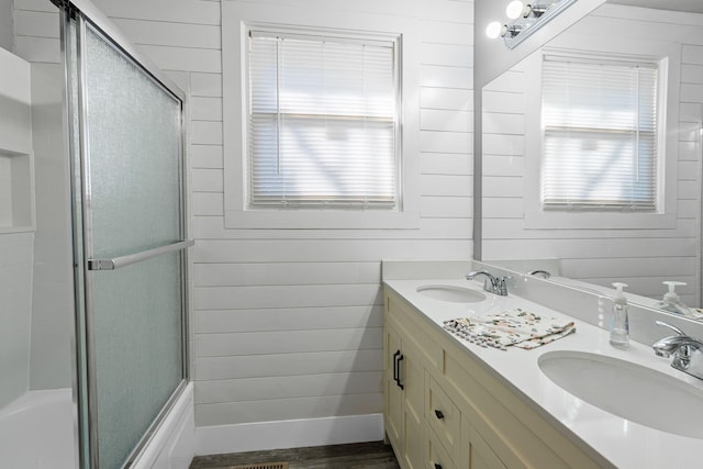 bathroom featuring bath / shower combo with glass door, vanity, and wooden walls