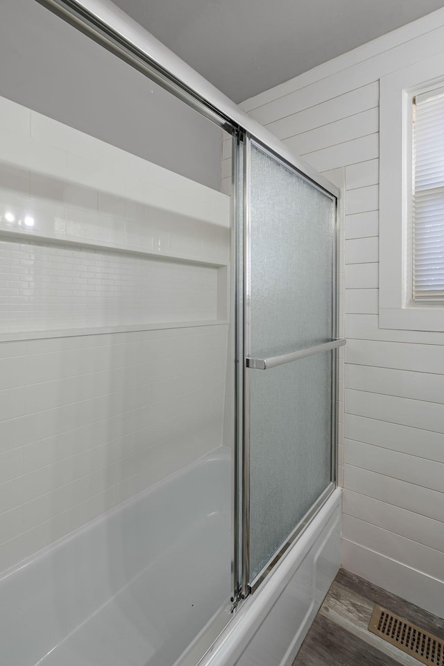 bathroom with shower / bath combination with glass door, hardwood / wood-style floors, and wood walls