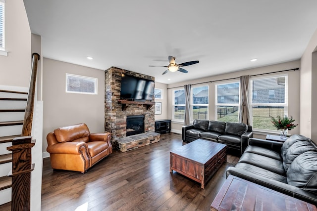 living room with ceiling fan, dark hardwood / wood-style flooring, and a stone fireplace