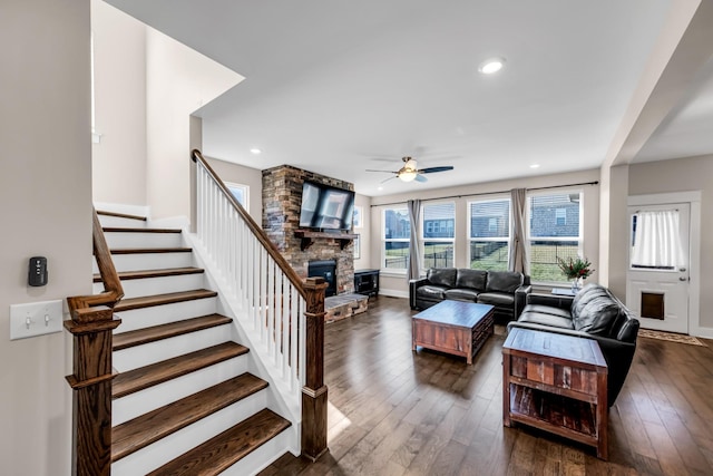 living room featuring ceiling fan, dark hardwood / wood-style flooring, and a stone fireplace