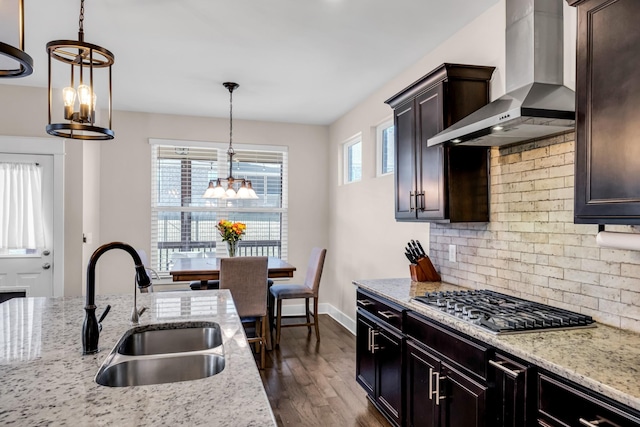 kitchen with dark brown cabinets, sink, wall chimney range hood, and light stone counters