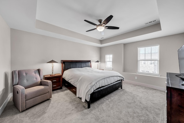 carpeted bedroom with ceiling fan and a raised ceiling