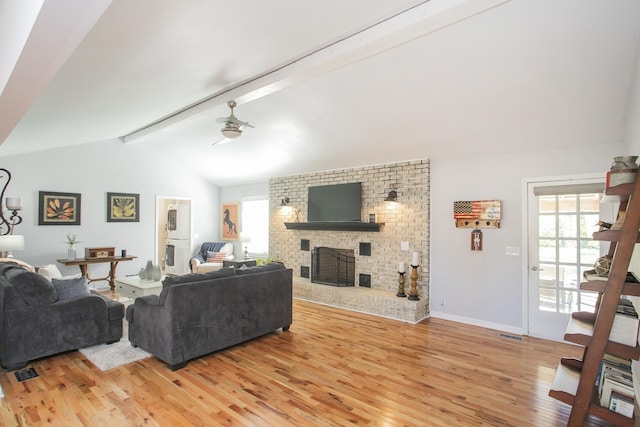 living room featuring ceiling fan, a brick fireplace, light hardwood / wood-style flooring, and vaulted ceiling with beams