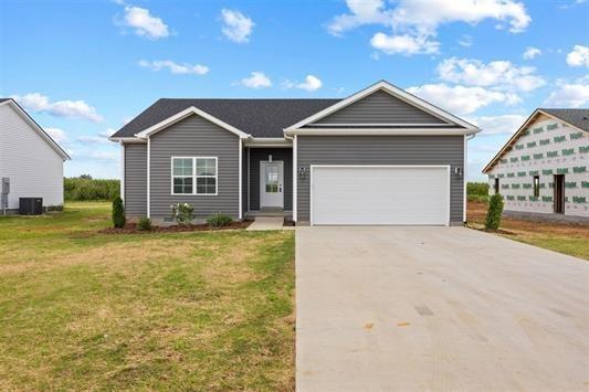 ranch-style home with driveway, central AC unit, an attached garage, and a front yard