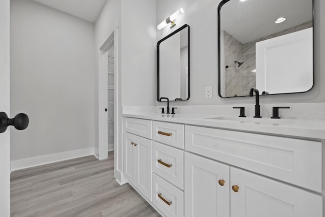 bathroom with wood finished floors, a sink, baseboards, double vanity, and walk in shower