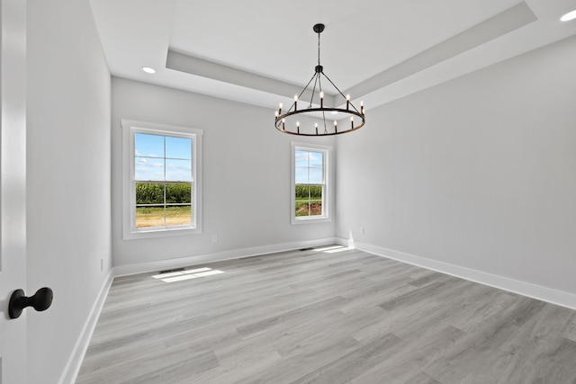 spare room with light wood finished floors, recessed lighting, a raised ceiling, a chandelier, and baseboards