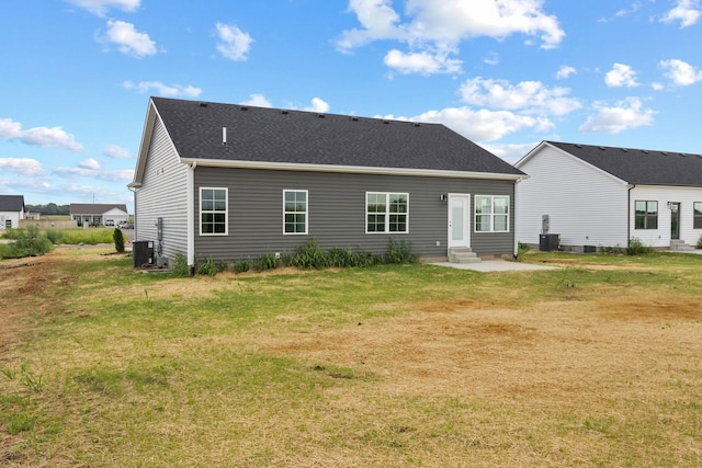 rear view of house with a shingled roof, entry steps, central AC, and a lawn