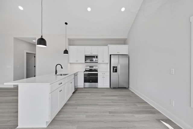 kitchen featuring light wood-style flooring, appliances with stainless steel finishes, a peninsula, light countertops, and a sink