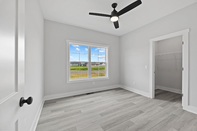 unfurnished bedroom featuring a spacious closet, a ceiling fan, light wood-style flooring, and baseboards