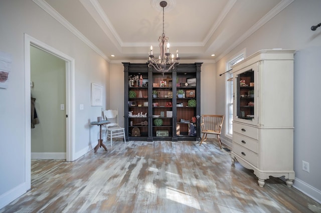 interior space with a raised ceiling, an inviting chandelier, wood finished floors, and ornamental molding