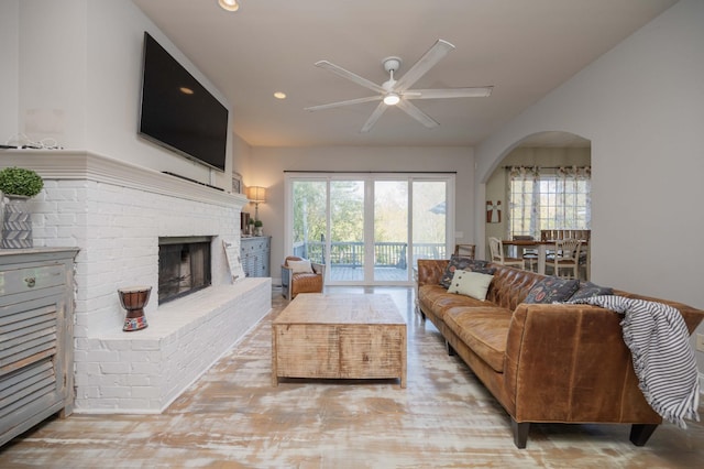 living area featuring recessed lighting, arched walkways, lofted ceiling, a brick fireplace, and ceiling fan