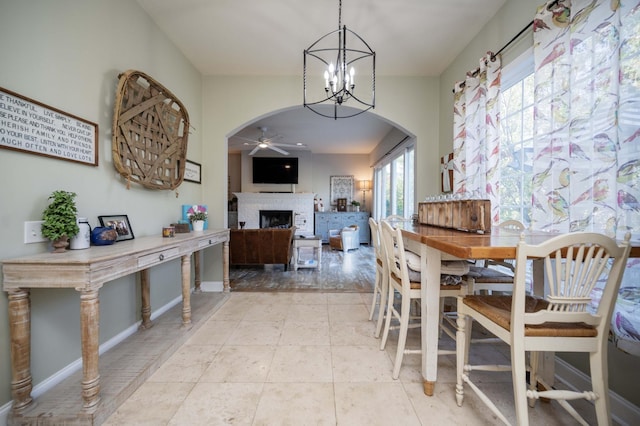 dining space with a ceiling fan, arched walkways, a fireplace, light tile patterned floors, and baseboards