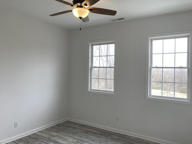 empty room with visible vents, plenty of natural light, baseboards, and wood finished floors