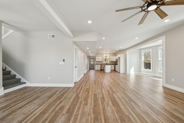 unfurnished living room featuring beamed ceiling, light hardwood / wood-style floors, and ceiling fan