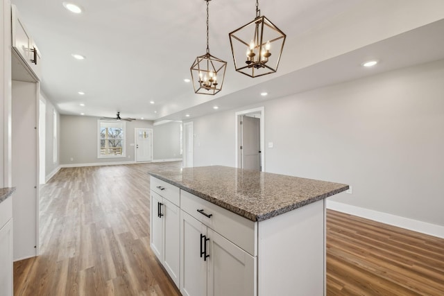 kitchen featuring pendant lighting, white cabinetry, wood-type flooring, dark stone countertops, and a center island