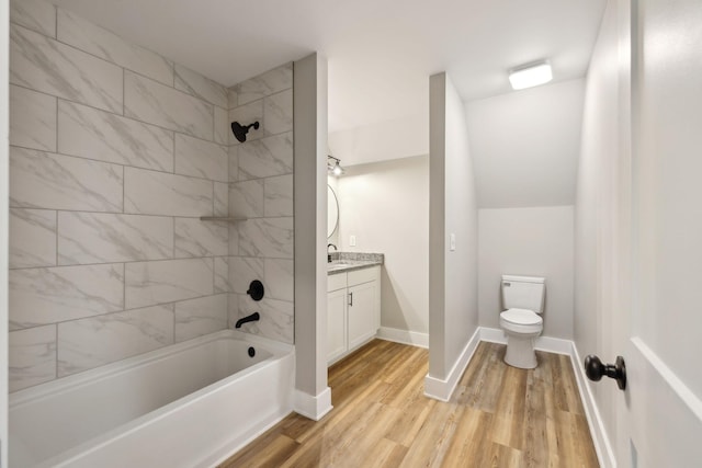 full bathroom featuring hardwood / wood-style flooring, vanity, tiled shower / bath, vaulted ceiling, and toilet