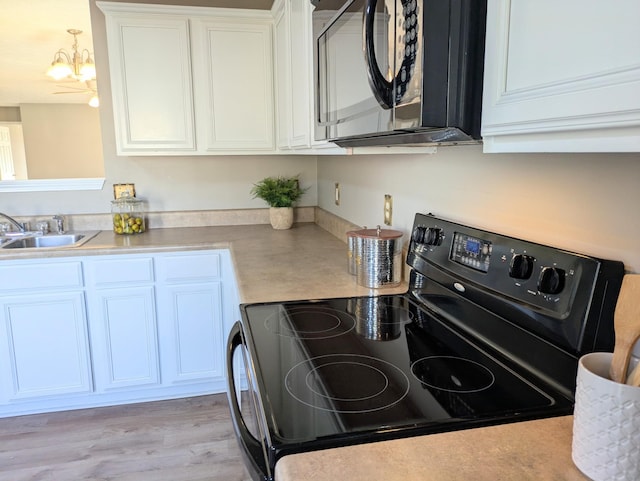 kitchen with sink, white cabinets, a notable chandelier, black appliances, and light wood-type flooring