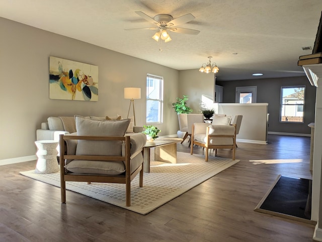 living area with dark wood-type flooring, ceiling fan with notable chandelier, and a textured ceiling