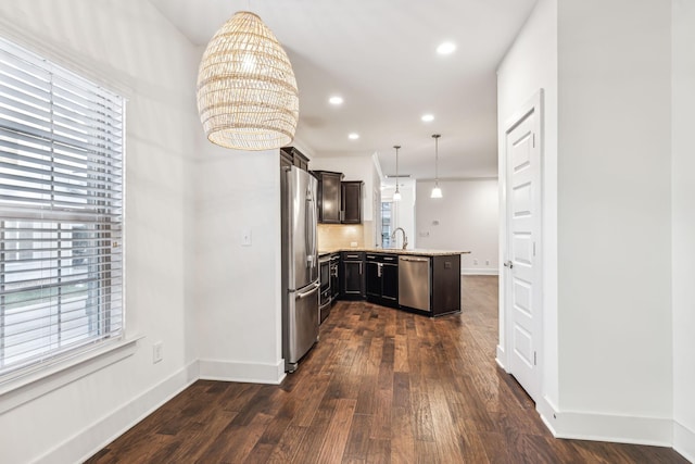 kitchen featuring dark wood-type flooring, sink, appliances with stainless steel finishes, kitchen peninsula, and pendant lighting