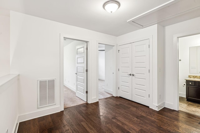 unfurnished bedroom with connected bathroom, dark wood-type flooring, and a closet