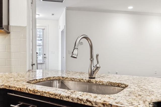 interior details featuring light stone counters, crown molding, sink, and backsplash