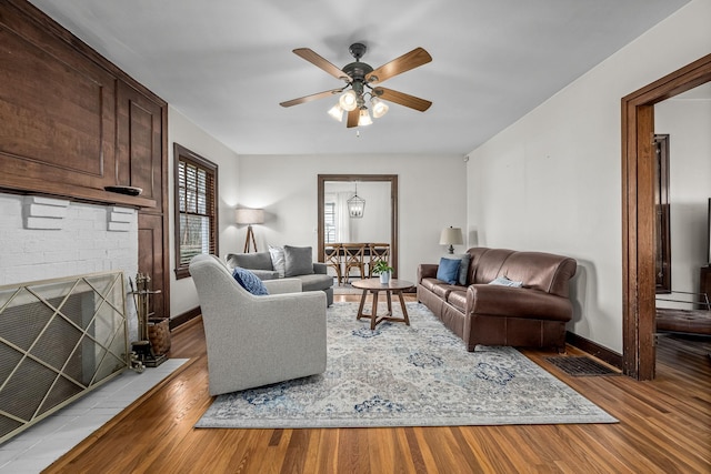 living room with ceiling fan, a brick fireplace, and light wood-type flooring